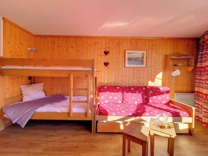 A wooden room with bunk beds, a sofa, a table, and a lamp. - travelski home classic - Résidence Grande Masse - Studio 3 personnes 709 (Les Menuires)