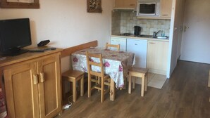 A compact kitchen with a microwave, stove, and sink. There's a dining table with chairs and a TV on a wooden cabinet. - travelski home classic - Résidence Grande Masse - Studio 3 personnes 709 (Les Menuires)