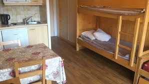 A bunk bed with a wooden headboard, a small table with a floral tablecloth, a chair, a kitchen area with a microwave, and a sink. - travelski home classic - Résidence Grande Masse - Studio 3 personnes 709 (Les Menuires)