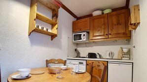 Eine kleine Küche mit Holzschränken, einer Mikrowelle, einer Kaffeemaschine und einem Kühlschrank.