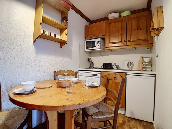 Una cocina compacta con armarios de madera, un microondas, una cafetera y un refrigerador.