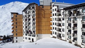 Ein modernes, mehrstöckiges Hotel mit Holzverkleidung und Balkonen, vor einer verschneiten Berglandschaft.