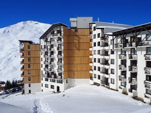 Ein modernes, mehrstöckiges Hotel mit Holzverkleidung und Balkonen, vor einer verschneiten Berglandschaft.