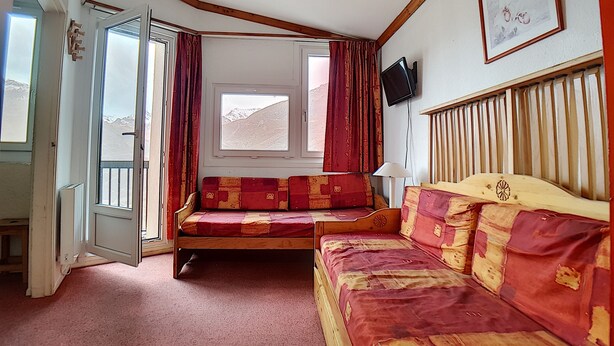 Ein Zimmer mit einem hölzernen Bett, einer Couch, einem Fenster mit Bergblick und einem an der Wand befestigten Fernseher.