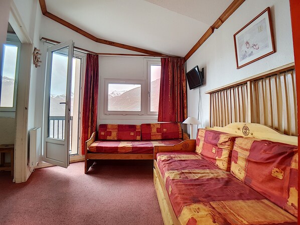 Ein Zimmer mit einem hölzernen Bett, einer Couch, einem Fenster mit Bergblick und einem an der Wand befestigten Fernseher.