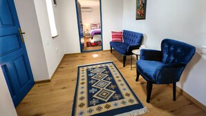 Una habitación con una puerta azul, dos sillones azules, un tapete estampado y un cuadro en la pared.