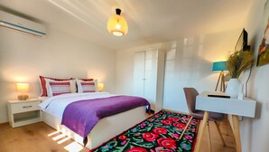 Un dormitorio con una cama, mesitas de noche, un escritorio, una silla y una alfombra colorida.