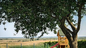 Un parque infantil con un tobogán y una casita de madera, rodeado de césped y una valla.
