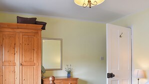 Et soveværelse med et træskab, en seng med hvide sengetøj, et natbord med en lampe, og en dør med håndtag.