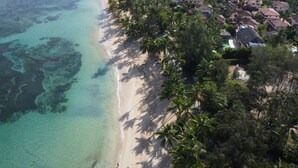 An aerial view of a beach with clear turquoise waters, a sandy shore, and a cluster of houses with red-tiled roofs. - 5 bedroom villa, large swimming pool 250m from the sea (Las Terrenas)