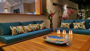 A modern living room with teal sofas, colorful tropical pillows, a wooden coffee table, and a large mirror. - 5 bedroom villa, large swimming pool 250m from the sea (Las Terrenas)