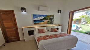 A bedroom with a bed, a painting of a beach scene, a wooden door, and a view of a pool and garden outside. - 5 bedroom villa, large swimming pool 250m from the sea (Las Terrenas)