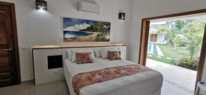 Quarto com cama, pintura de uma praia e vista para o jardim e piscina.