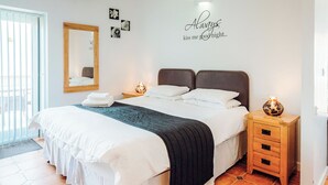 A hotel room with a bed, bedside tables, a mirror, a wall with a 'Always kiss me good night' sign, and a tiled floor. - Greenkeepers Cottage - UK6712 (Lydstep, near Tenby)