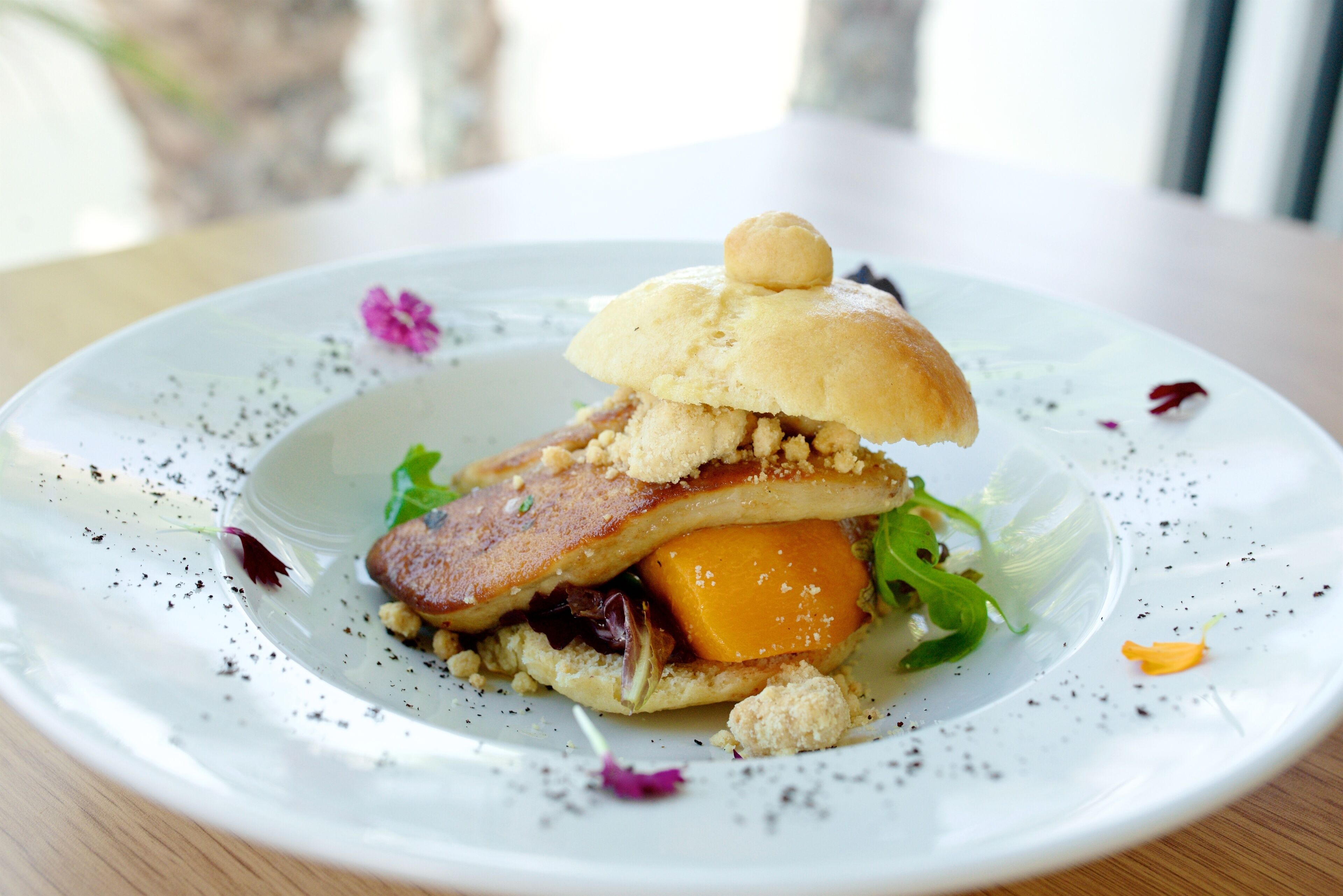 Un plato con un sándwich, ensalada y una flor decorativa.