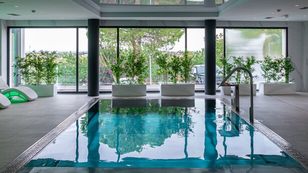 An indoor swimming pool with clear glass walls, potted plants, and modern seating. - Syncrosfera Fitness & Spa Health Hotel Boutique (Pedreguer)