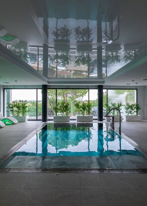 Une piscine intérieure avec des parois en verre transparent, des plantes en pot et des sièges modernes.