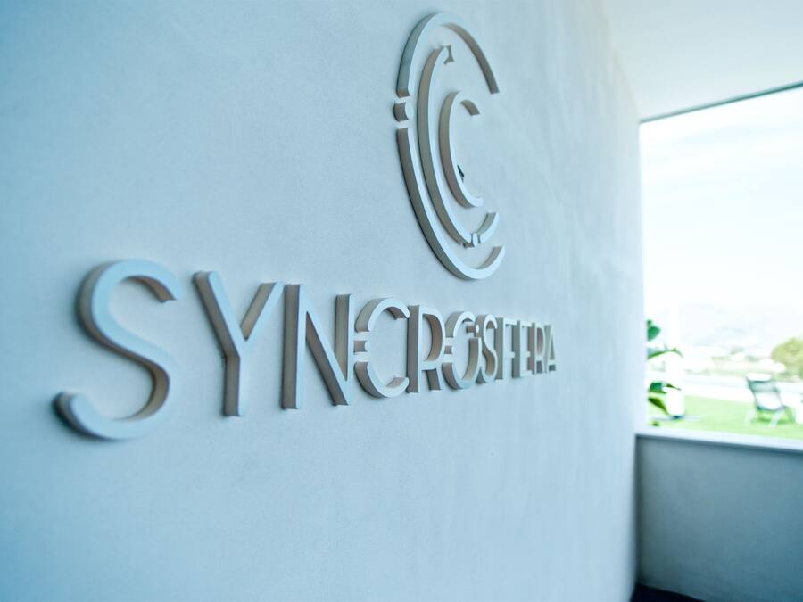 A wall with the words "SYNCROSTERA" and a stylized 'C' logo.