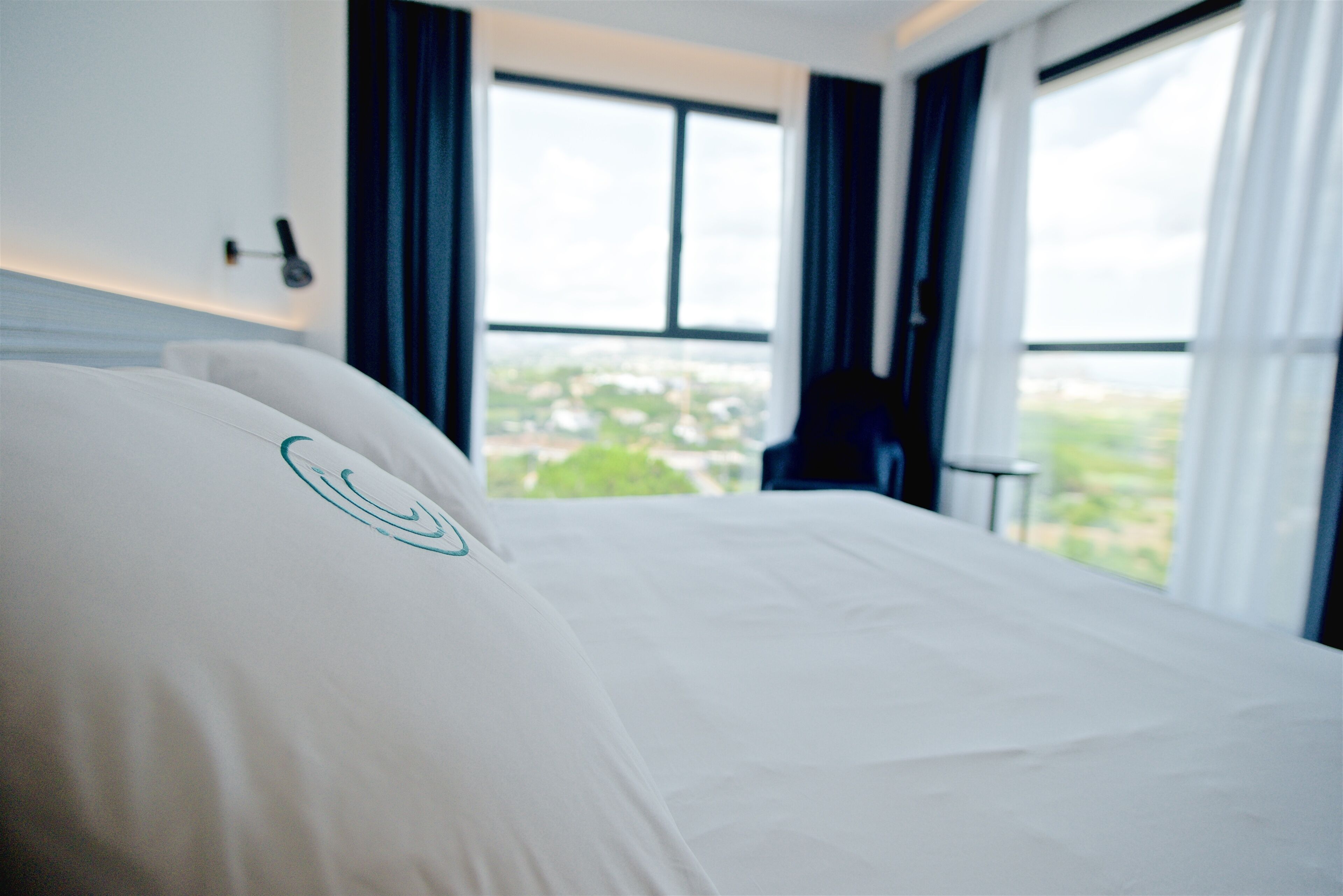 Een hotelkamer met een bed, grote ramen en uitzicht op de stad.