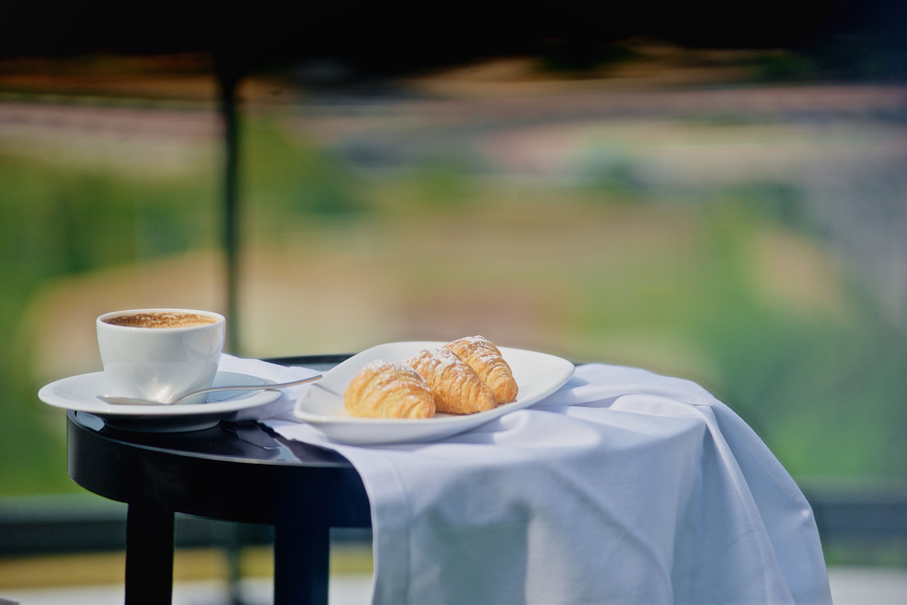 Ein Tisch mit weißer Tischdecke, einer Tasse Kaffee und einem Teller mit Croissants.