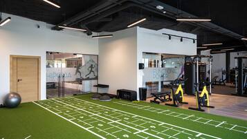 Un gimnasio con zona de césped artificial verde, equipo de ejercicio y una pared con letrero de máquina funcional.