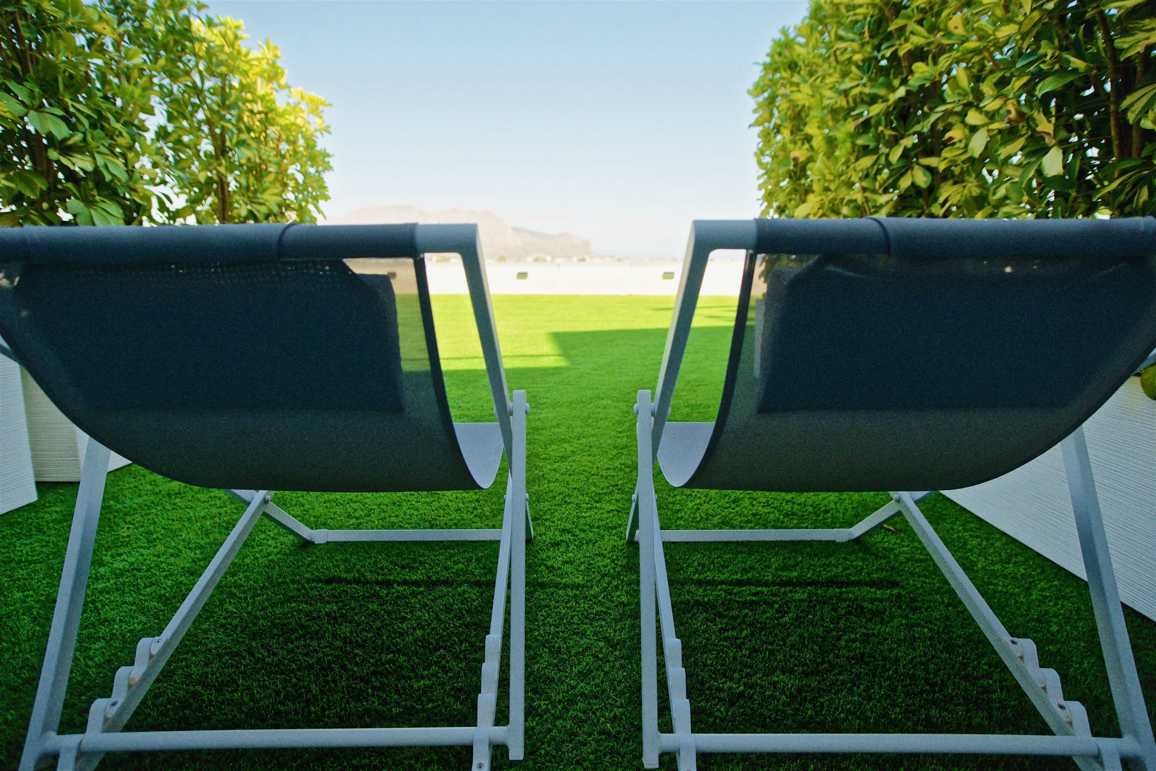 Two lounge chairs facing a green lawn with a white fence and trees in the background.