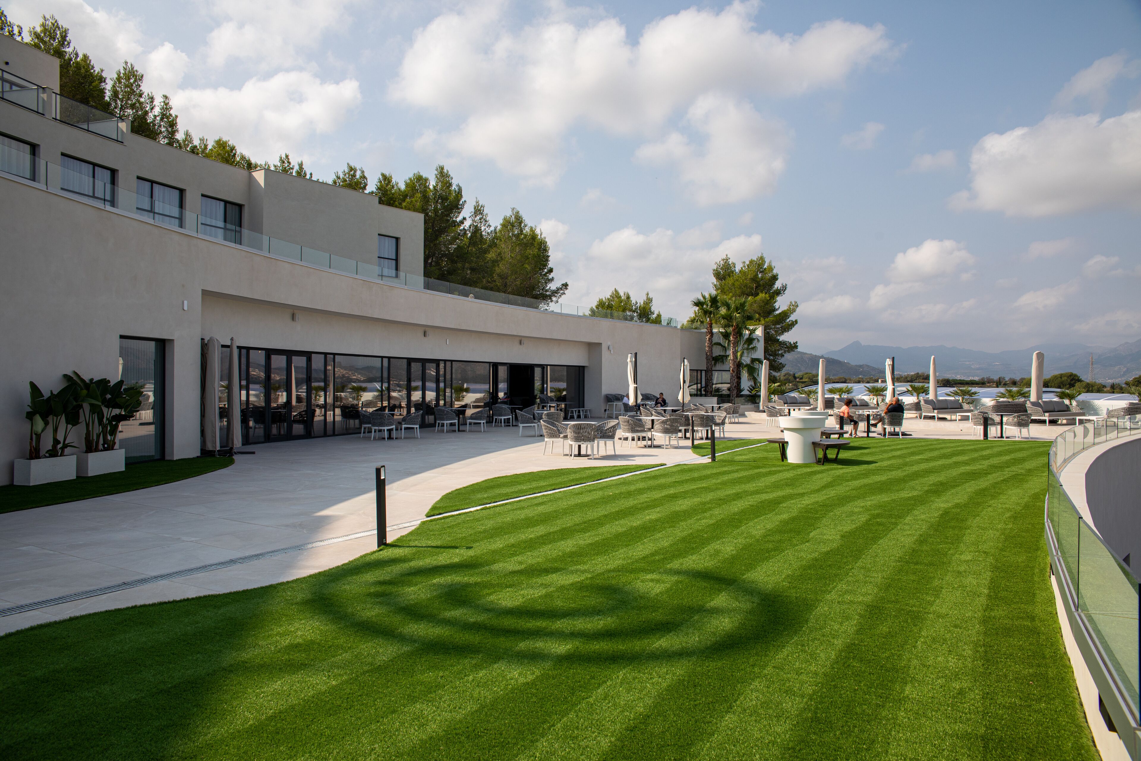A modern building with a flat roof, large windows, and a well-maintained lawn with outdoor seating.