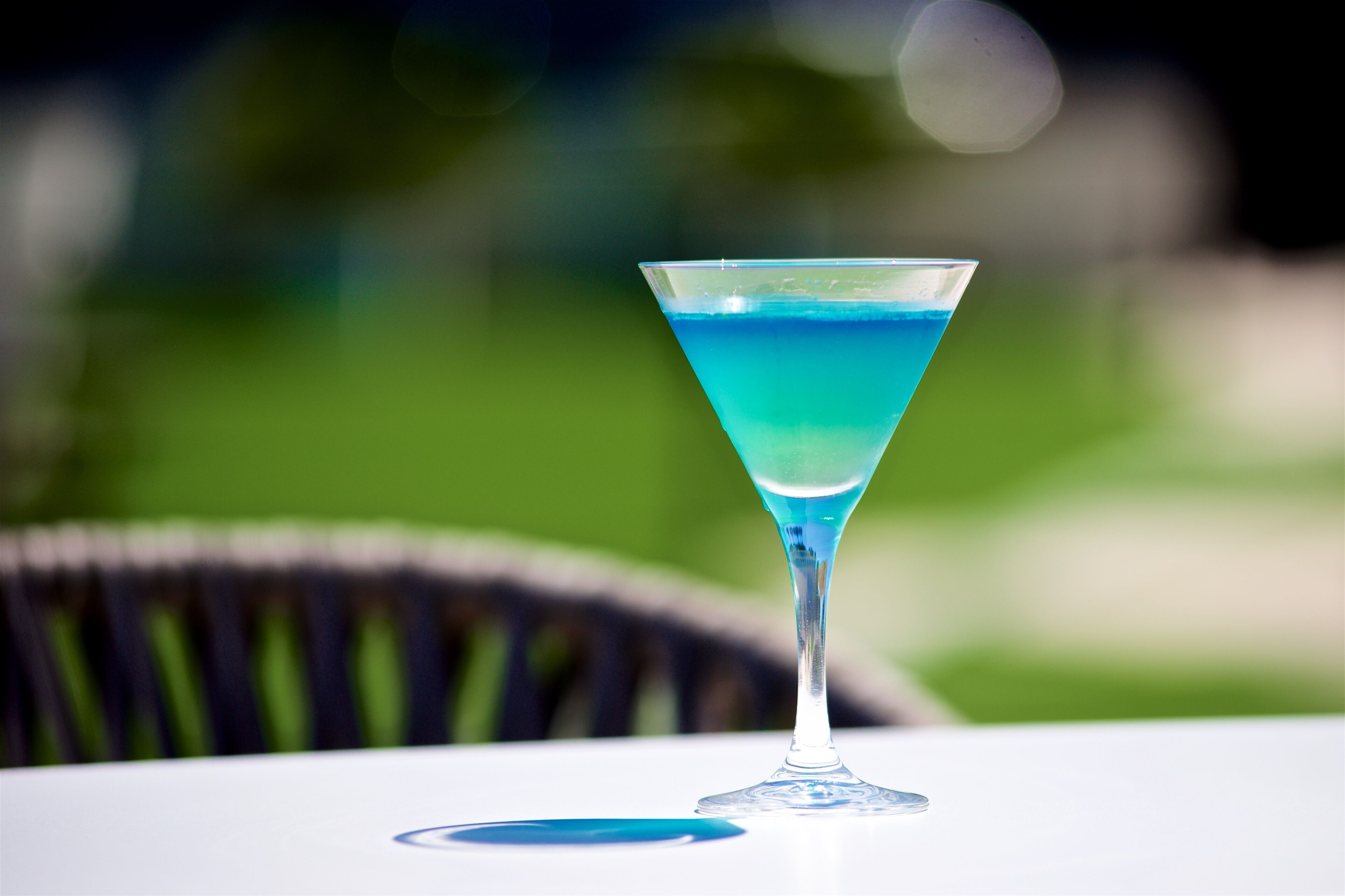 A martini glass with a blue liquid on a white table.