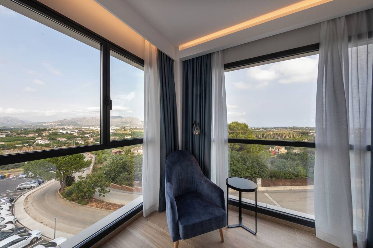 Une pièce moderne avec une grande fenêtre, un fauteuil sombre et une petite table.