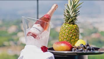 Una copa de champán en un balde, una piña, una rosa roja, un mango y un plato con uvas y un limón.