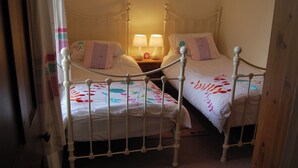 A room with two beds, each with a white metal frame and floral bedding. There is a bedside table with a lamp and a clock between the beds. - 3 bedroom accommodation in Silverdale near Grange Over Sands (Silverdale near Grange Over Sands)