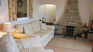 A living room with a beige sofa, a lamp, a stone fireplace, and a clock on the wall. - 3 bedroom accommodation in Silverdale near Grange Over Sands (Silverdale near Grange Over Sands)