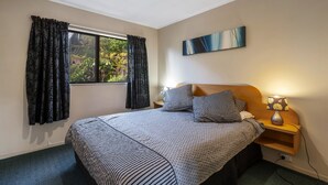Une chambre à coucher avec un lit, deux oreillers, une table de chevet avec une lampe, une fenêtre avec des rideaux et un tableau au mur.
