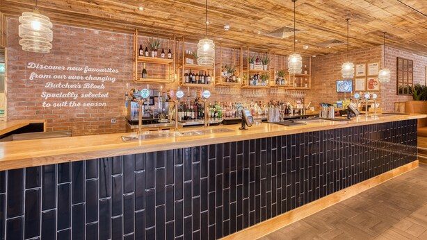 Eine Bar mit Holzbalkendecke, Regalen voller Flaschen und einer Theke mit Registrierkasse.