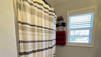 A bathroom with a striped shower curtain, a toilet, a rug, and a window with blinds.