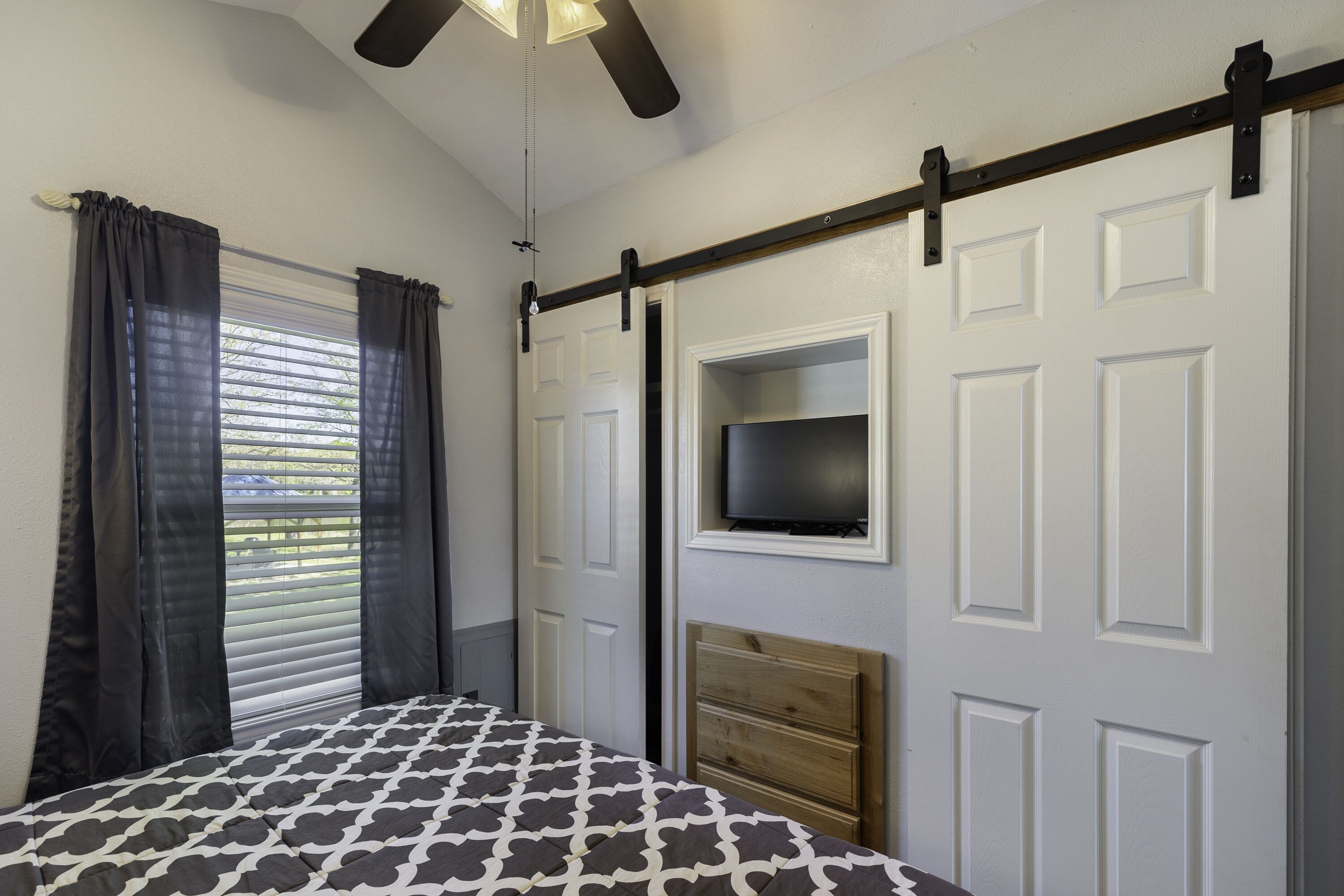 A bedroom with a bed, a TV mounted on the wall, a ceiling fan, and a sliding door.
