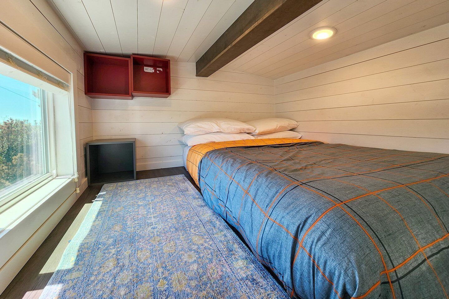 Un dormitorio con cama, ventana, chimenea y un mueble pequeño.