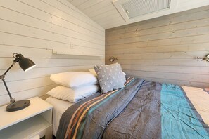A bedroom with a wooden slat ceiling, a bed with striped bedding, white pillows, and a desk with a lamp. - Big Stump (Lincoln County)