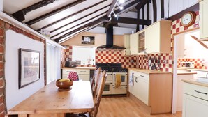 A kitchen with a wooden table and chairs, a stove, and a microwave. - The Old Custom House (Halesworth)