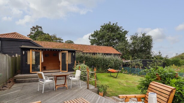 Una terraza de madera con mobiliario exterior, un pequeño patio y un jardín con una hamaca.