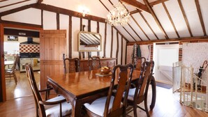 A dining area with a wooden table and chairs, a chandelier, and a kitchen in the background. - The Old Custom House (Halesworth)