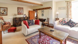 A spacious living room with two white sofas, a glass coffee table, and a red patterned rug. - The Old Custom House (Halesworth)