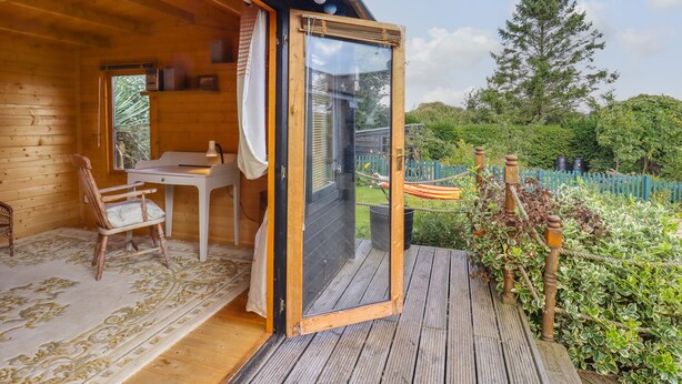 A wooden cabin with a glass door leading to an outdoor deck. Inside, there is a desk with a chair and a small table. - The Old Custom House (Halesworth)