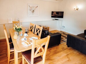 A dining area with a wooden table set for two, a coffee pot, and a vase of flowers.