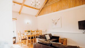 A living room with a wooden ceiling, a black leather sofa, a dining table with chairs, and a mounted TV. - Goose Cottage- UK6737 (Lydstep, near Tenby)