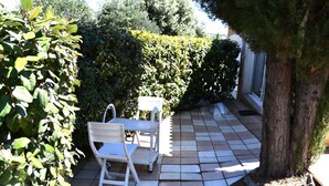 A patio with a white table and chair, surrounded by greenery and a tiled floor. - Independent 25m2 studio in Villa: Wi-fi + terrace (Saint-Gély-du-Fesc)