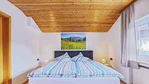 Une chambre avec un plafond en bois, un lit avec une literie à rayures, deux lampes de chevet et une fenêtre avec des rideaux.