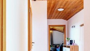 Un couloir au plafond en bois et au sol carrelé, qui mène à un espace de vie comprenant un canapé et un téléviseur.