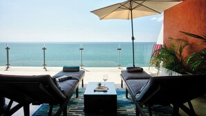 En terrasse med to liggestole, et bord og en parasol med udsigt over havet.