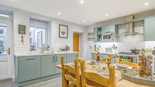A modern kitchen with light blue cabinets, a wooden dining table, and a central island with a coffee machine. - 2 bedroom accommodation in Coniston (Coniston)